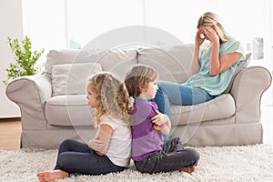 Angry siblings sitting arms crossed with upset mother on sofa