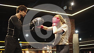 Angry sport woman training with coach at gym. Fit girl fighting on boxing ring