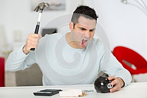 angry sreaming young man wearing trying to break piggy bank