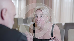 Angry stressed blond woman yelling at bald man in cafe. Portrait of dissatisfied nervous Caucasian lady shouting and