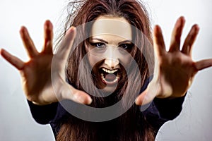 Angry, stressed, frightened and screaming mad young woman in black against light background.