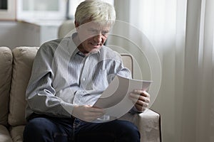 Angry stressed senior man staring at document, reading paper letter