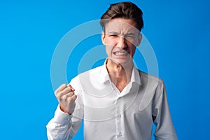 Angry stressed teen boy with clenched fist on blue background