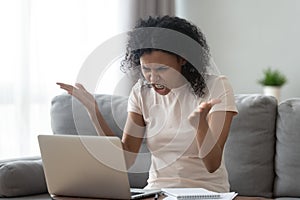 Angry stressed young black woman looking at laptop feeling annoyed