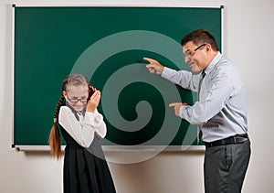 Angry teacher shout to schoolgirl, posing at blackboard background - back to school and education concept
