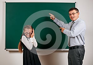 Angry teacher shout to schoolgirl, posing at blackboard background - back to school and education concept