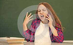 angry teen girl speaking on mobile phone in high school at blackboard, conversation