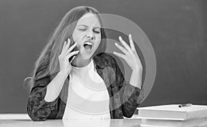 angry teen girl speaking on mobile phone in high school at blackboard, conversation