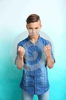 Angry teenage boy with clenched fists on color background