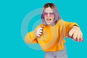 Angry teenager with brass knuckles hits camera on blue background. Pubertal journey of adolescence.