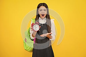 Angry teenager girl, upset and unhappy negative emotion. Back to school. Teenager school girl with backpack hold clock