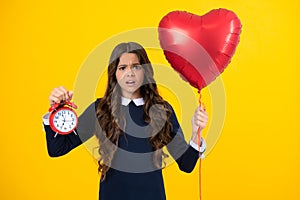 Angry teenager girl, upset and unhappy negative emotion of teen student girl with clock isolated on yellow background