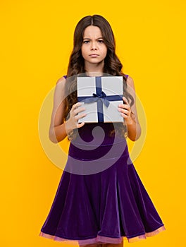 Angry teenager girl, upset and unhappy negative emotion. Teenager child holding gift box on yellow  background