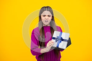 Angry teenager girl, upset and unhappy negative emotion. Teenager child holding gift box on yellow isolated background