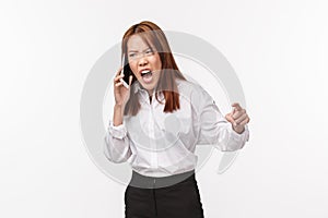 Angry and tensed, aggressive young asian woman cursing as talking on phone, clench fist outraged screaming in mobile