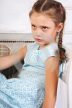 Angry thinking kid girl sitting on the bench in blue dress and l