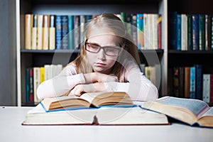 Angry and tired schoolgirl studying with a pile of books