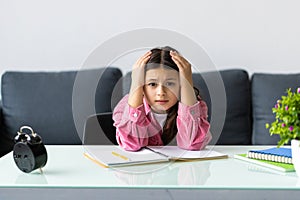 Angry and tired teen schoolgirl studying with a pile of books on her desk