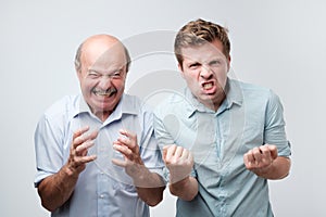 angry two men exclaim with negative emotions shout loudly, over white studio wall. Annoyed son and father have failure