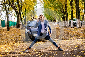 Angry upset businessman in suit emotionally swears on the phone near the car.