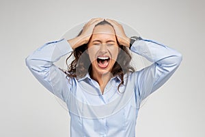 Angry upset despaired young caucasian woman in formal wear screams, freaking out, hold head with hands