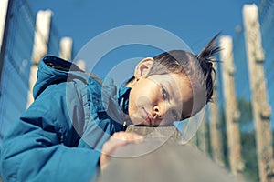 Angry and upset little boy leaning his head on wooden railing