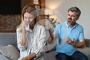 Angry upset mature european husband yells at crying wife, couple quarreling in living room interior