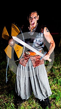 Angry Viking warrior with black war paint, openig his mouth and holding his sword.