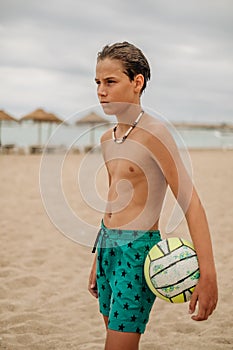 Angry wet boy holding volleyball ball on the beach