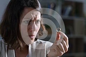 Angry wife looking at wedding ring at night at home