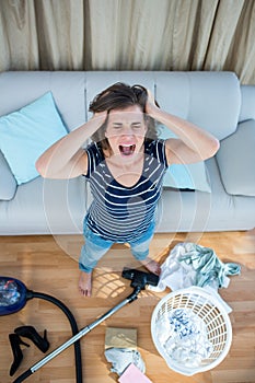 Angry woman in a chaotic living room with vacuum cleaner