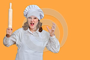 Angry woman chef with dough rolling pin in hand on studio background, copy space