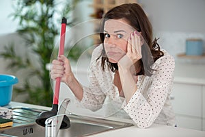 Angry woman cleaning pipe with cup plunger