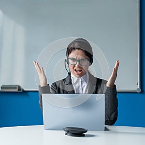 An angry woman in a headset is having an online conversation on a laptop in a conference room. Female boss scolding