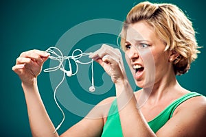 Angry woman holding tangled earphone trying to untangle it. People and technology concept
