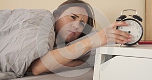 Angry woman keeping ringing alarm clock under the pillow