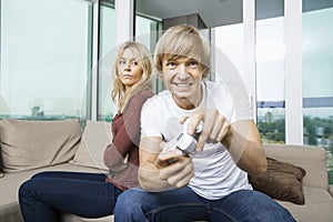 Angry woman looking at man play video game in living room at home
