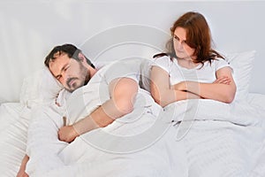 Angry woman looking at a man sleeping in a white bed, concept. Relationship problems coupled with isolation due to coronavirus