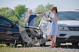 Angry woman and man drivers of heavily damaged vehicles calling insurance service for help in car crash accident on