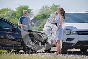 Angry woman and man drivers of heavily damaged vehicles calling insurance service for help in car crash accident on