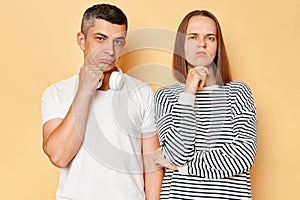 Angry woman and offended unhappy man wearing casual outfits standing isolated over beige background looking at camera different