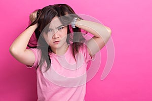 Angry woman screaming out and pulling her hair over pink background