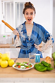 Angry woman screaming and waving rolling pin in home kitchen