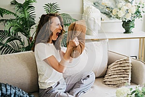 An angry woman screams into a pillow and slams her fists on the couch.