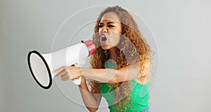 Angry woman, shouting and protest with megaphone for power, rights or equality on a gray studio background. Frustrated