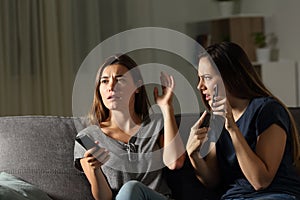 Angry woman showing phone and friend ignoring her photo