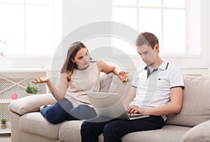 Angry woman sitting while husband using laptop