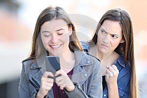 Angry woman spying her friend using phone