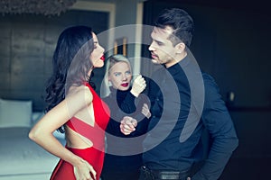 Angry woman threatens disloyal man flirting girl in red dress photo