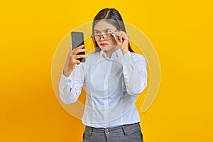 Angry young asian woman using mobile phone and taking glasses isolated over yellow background